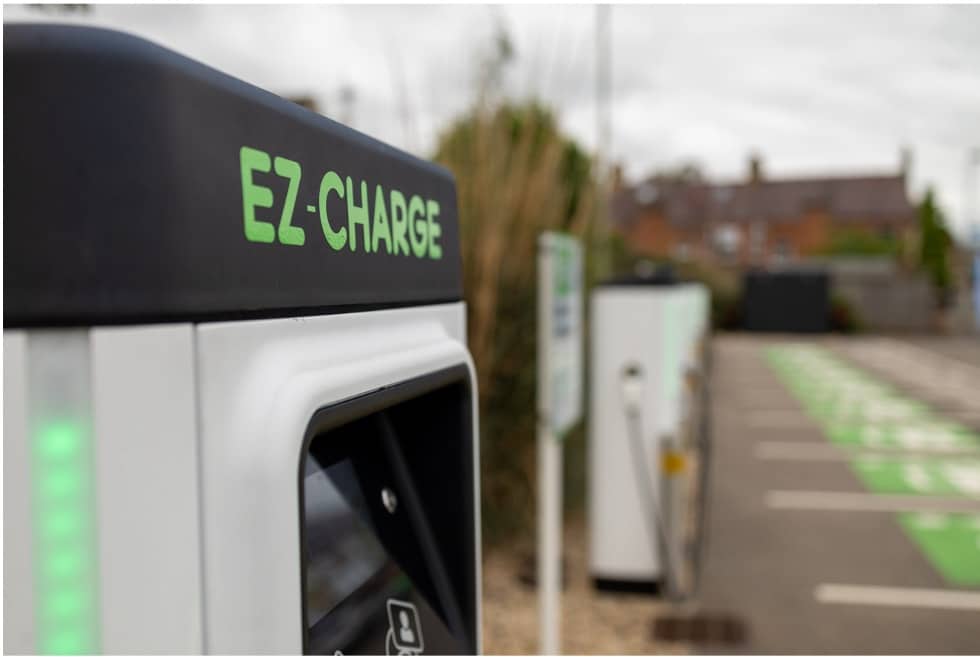 Close up of an electric vehicle charge point looking down a row of identical charge points. They are grey with black tops displaying 'EZ-CHARGE' in green font
