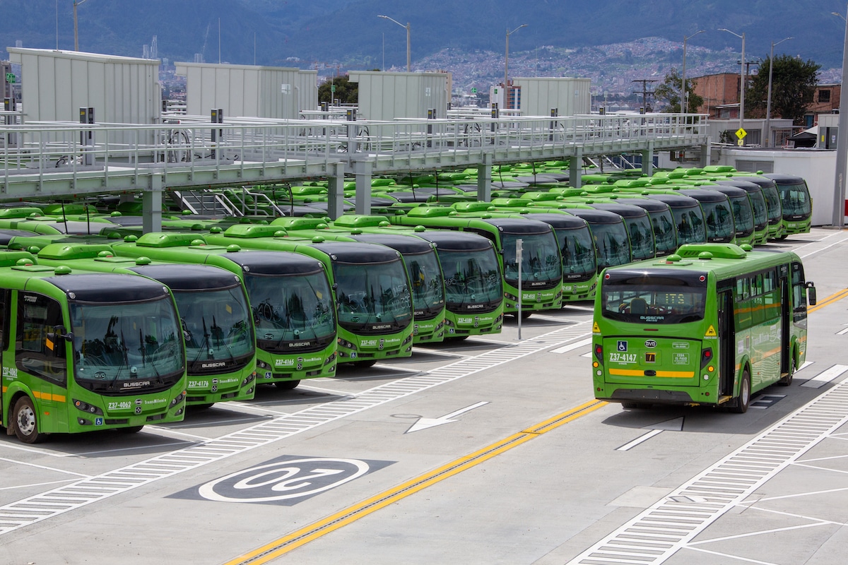 A large fleet of green electric buses at their Bogotá depot under their charging infrastructure, the result of a partnership between VG Mobility and TransMilenio