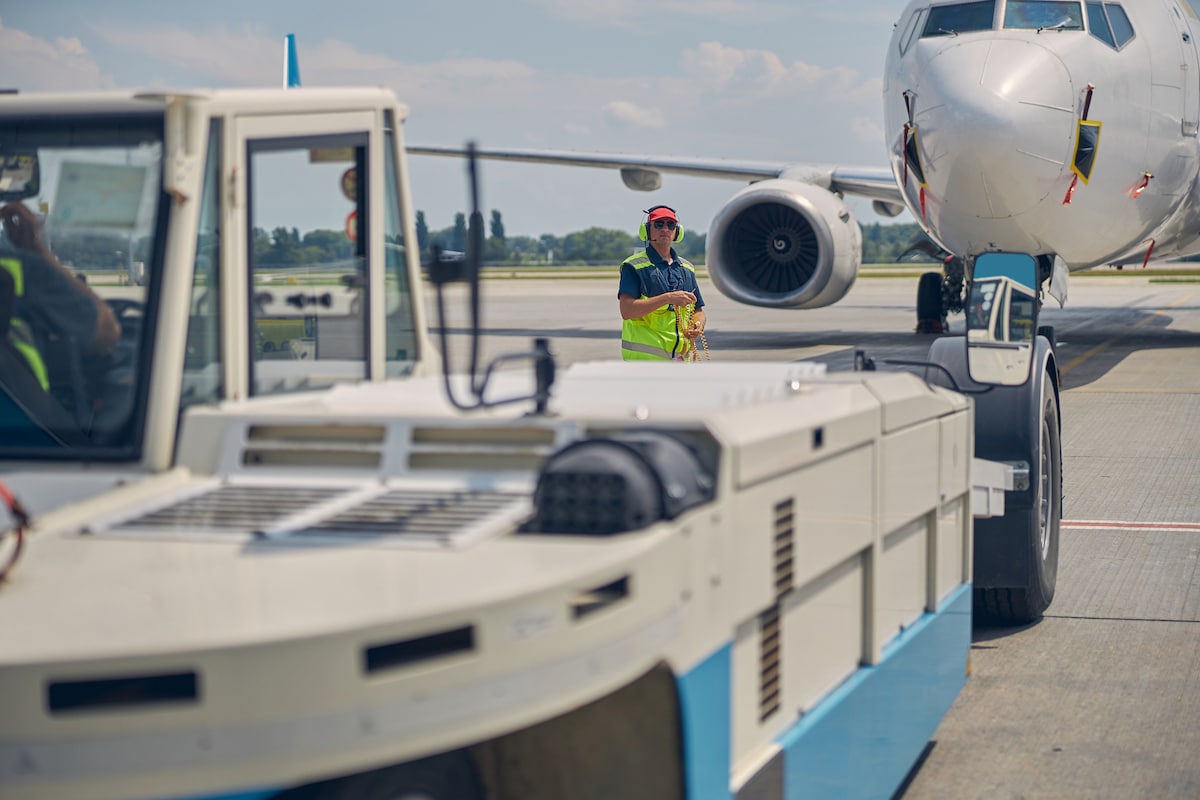 A member of ground crew prepares to tow a large commercial jet-engine aircraft using a pushback tractor