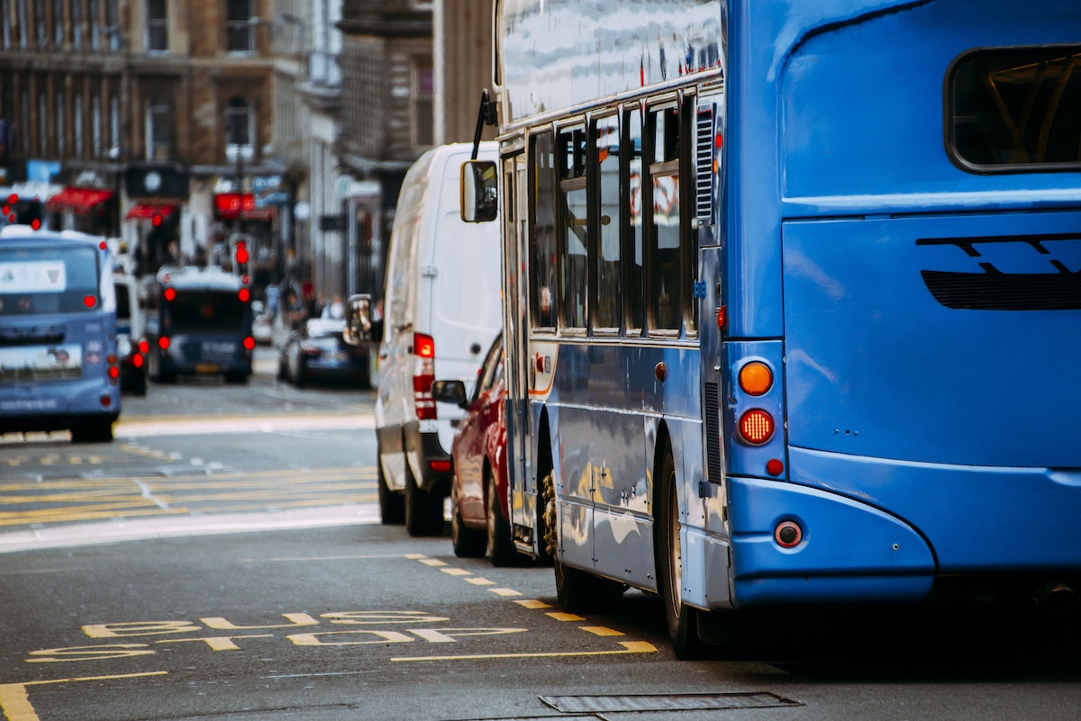A white LCV, a passenger car, and a bus queue in traffic in a major city